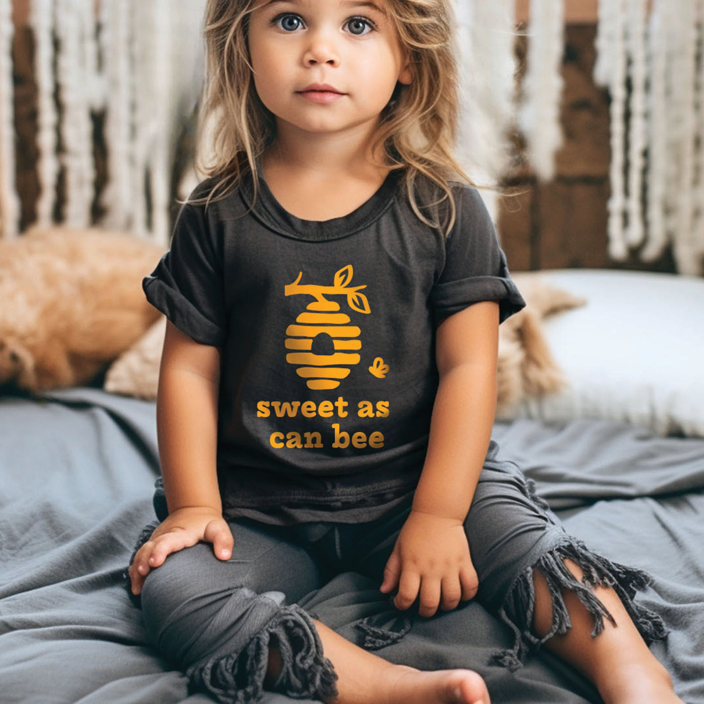 Little toddler girl wearing natural off white short sleeve toddler shirt with mustard yellow little sunshine with sun rays print, laying down on blanket in grass with sun hat